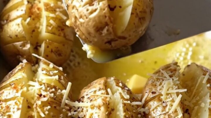 A top-down view of raw, accordion-cut russet potatoes in a white ceramic dish being drizzled with garlic butter.