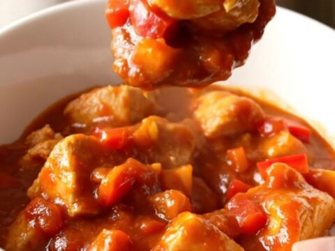 A close-up of a bowl filled with chicken and bell pepper stew in a rich tomato sauce.