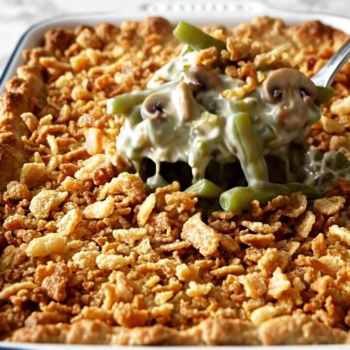 A top-down view of a rectangular white baking dish filled with raw green beans, creamy mushroom sauce, and crispy onions.