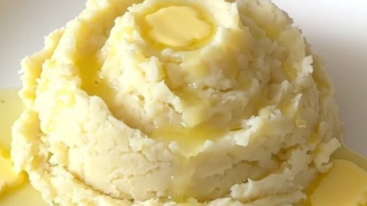 A top-down view of a slow cooker filled with cubed raw Yukon gold potatoes, cream cheese, and butter.
