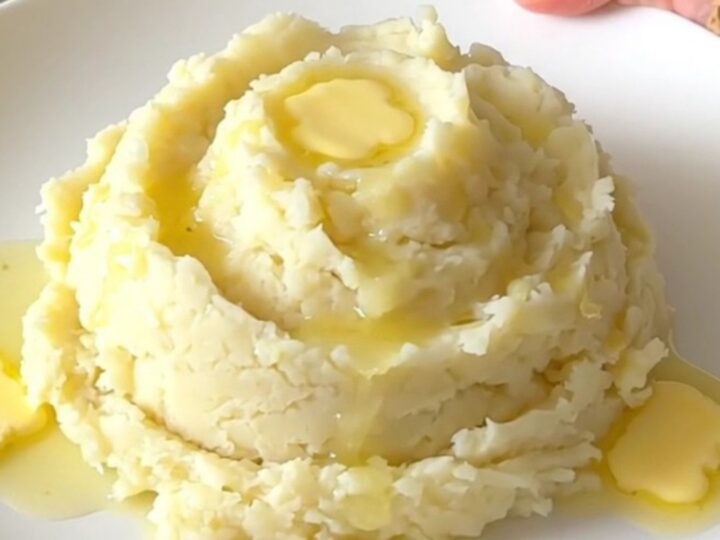 A top-down view of a slow cooker filled with cubed raw Yukon gold potatoes, cream cheese, and butter.