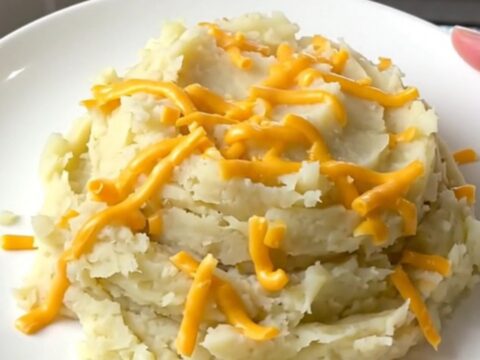 A close-up of creamy mashed potatoes in a slow cooker topped with melted cheddar cheese.