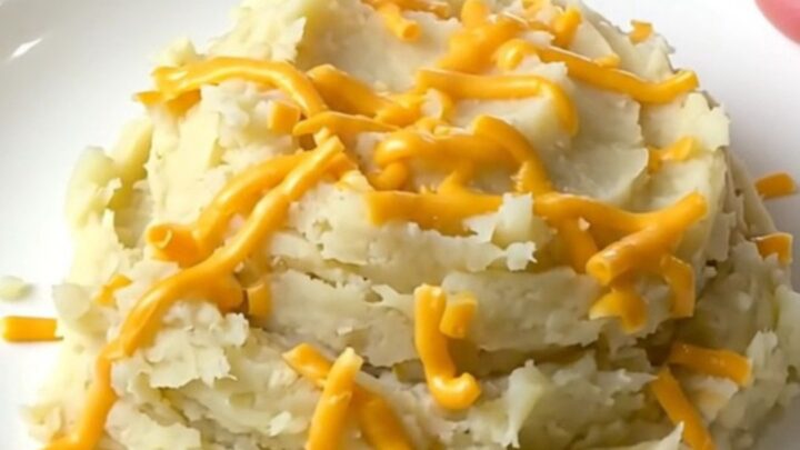A close-up of creamy mashed potatoes in a slow cooker topped with melted cheddar cheese.