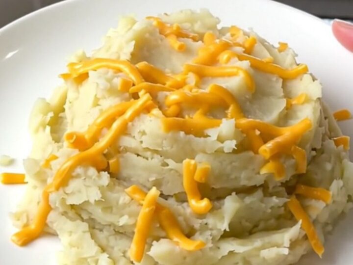A close-up of creamy mashed potatoes in a slow cooker topped with melted cheddar cheese.