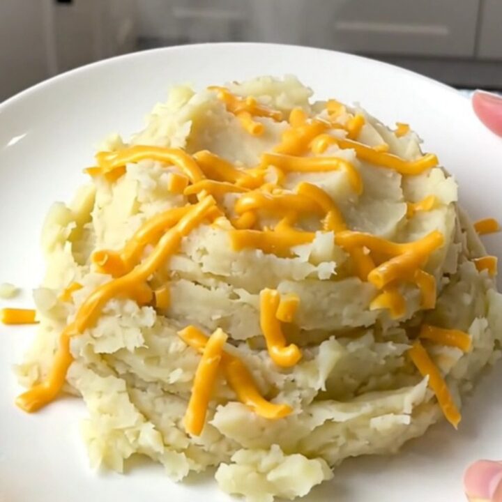 A close-up of creamy mashed potatoes in a slow cooker topped with melted cheddar cheese.