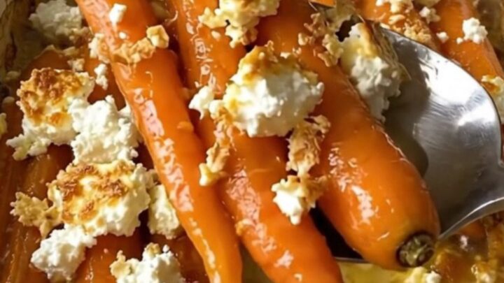 A large ceramic baking dish filled with roasted whole carrots glazed in honey butter and topped with crumbled feta cheese.