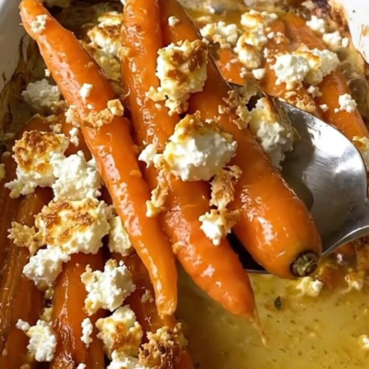 A large ceramic baking dish filled with roasted whole carrots glazed in honey butter and topped with crumbled feta cheese.