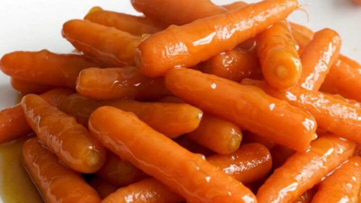 A stainless steel slow cooker filled with raw baby carrots, butter slices, and brown sugar before cooking.