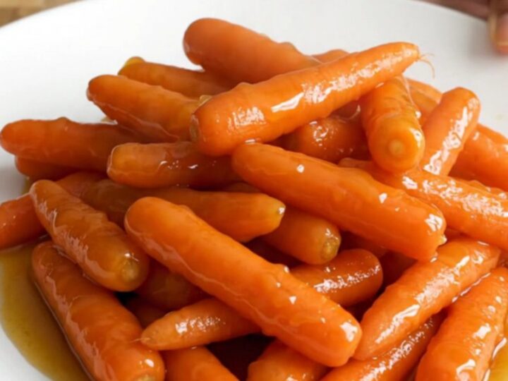 A stainless steel slow cooker filled with raw baby carrots, butter slices, and brown sugar before cooking.