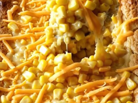 A golden, puffed sweet corn casserole in a white ceramic dish sitting on a warm beige countertop.
