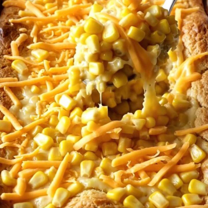 A golden, puffed sweet corn casserole in a white ceramic dish sitting on a warm beige countertop.