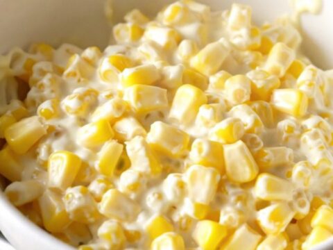 A close-up shot of creamy slow-cooked corn served in a white bowl with a gentle steam rising.