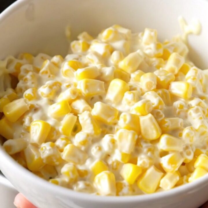 A close-up shot of creamy slow-cooked corn served in a white bowl with a gentle steam rising.