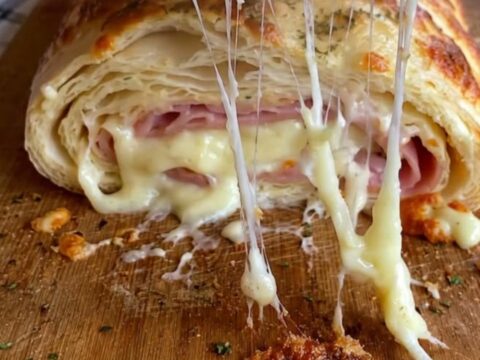 A golden, flaky ham and mozzarella stromboli sitting on a rustic wooden cutting board with warm light.