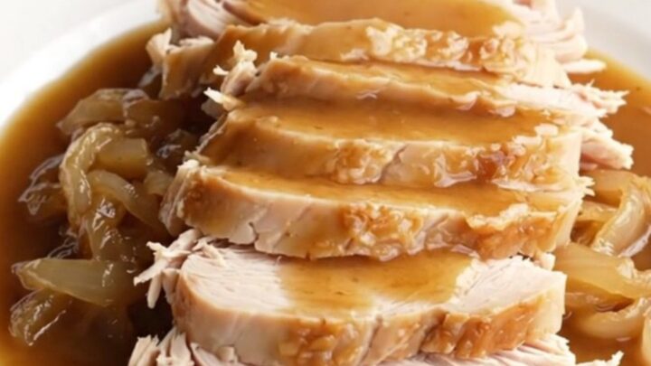 A succulent boneless turkey breast cooked in a slow cooker with rich brown gravy and onions.