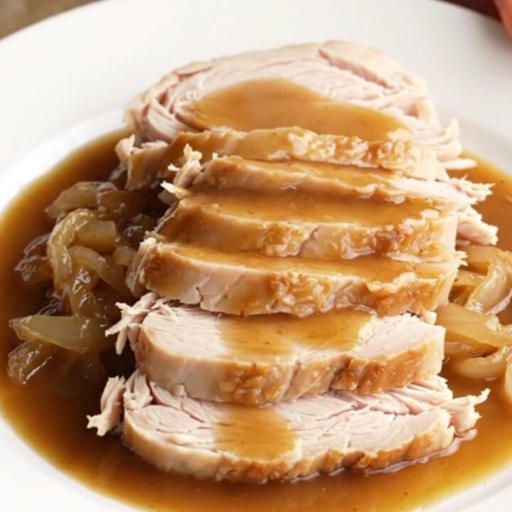 A succulent boneless turkey breast cooked in a slow cooker with rich brown gravy and onions.