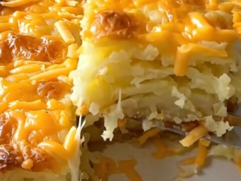 A large ceramic baking dish filled with golden-brown, cheesy scalloped potatoes on a wooden countertop.
