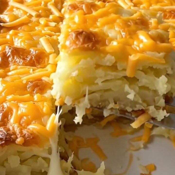 A large ceramic baking dish filled with golden-brown, cheesy scalloped potatoes on a wooden countertop.
