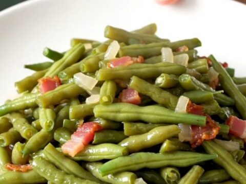 A top-down view of fresh green beans, bacon, and onions in a slow cooker before cooking.