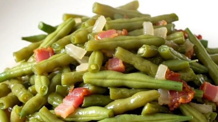 A top-down view of fresh green beans, bacon, and onions in a slow cooker before cooking.