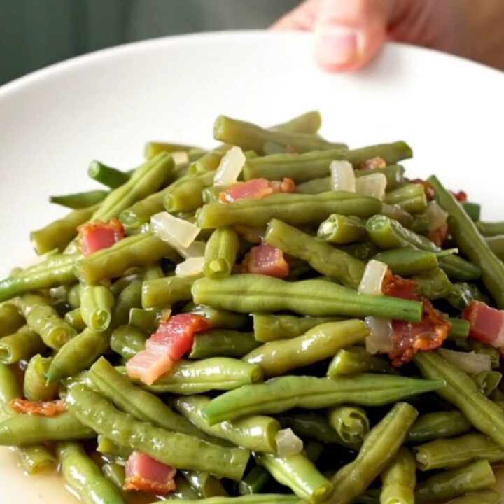 A top-down view of fresh green beans, bacon, and onions in a slow cooker before cooking.