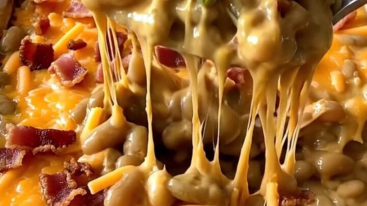 A top-down view of a rectangular baking dish filled with green beans, creamy cheddar sauce, bacon, and cheese.
