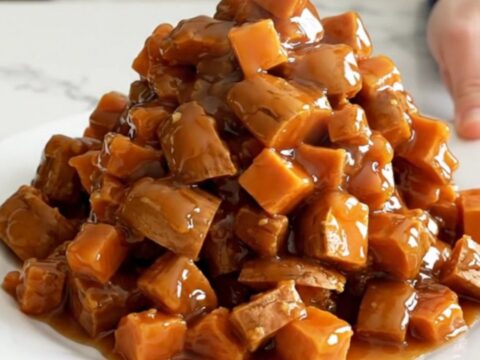A close-up of tender, caramelized sweet potato cubes in a dark slow cooker, covered in a glossy