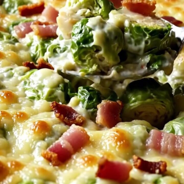 A top-down view of a rectangular baking dish filled with raw, halved Brussels sprouts and garlic cream.