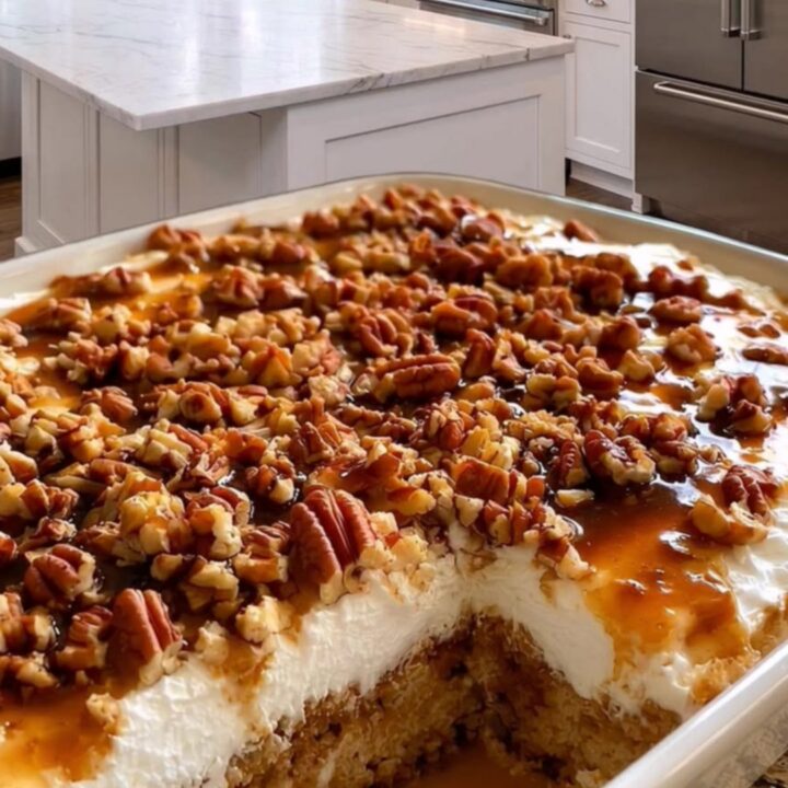 A slice of decadent pecan caramel poke cake on a plate showing layers of cake, caramel, and whipped cream.