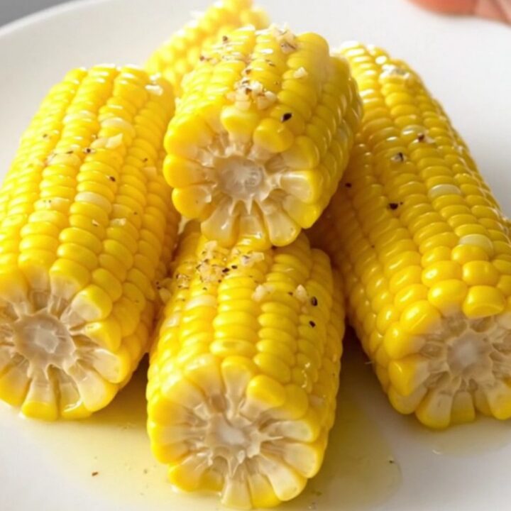 A top-down view of halved raw corn cobs being prepared in a black slow cooker insert.