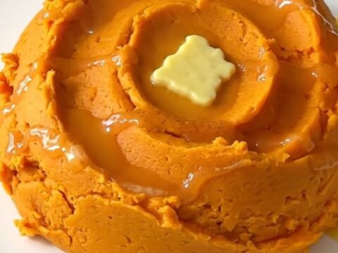 A mound of creamy, vibrant orange mashed sweet potatoes with cinnamon swirls in a ceramic bowl.