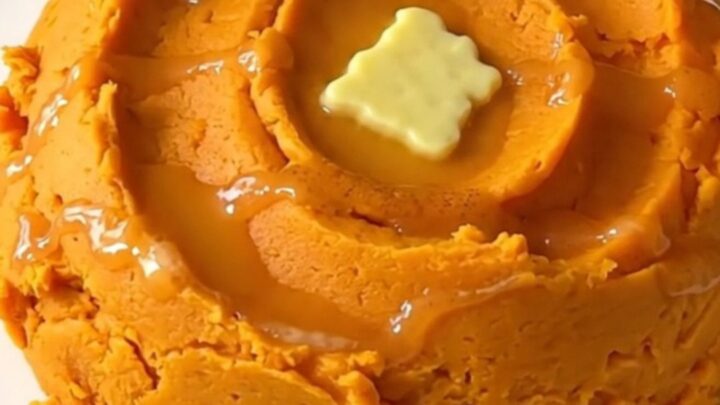 A mound of creamy, vibrant orange mashed sweet potatoes with cinnamon swirls in a ceramic bowl.