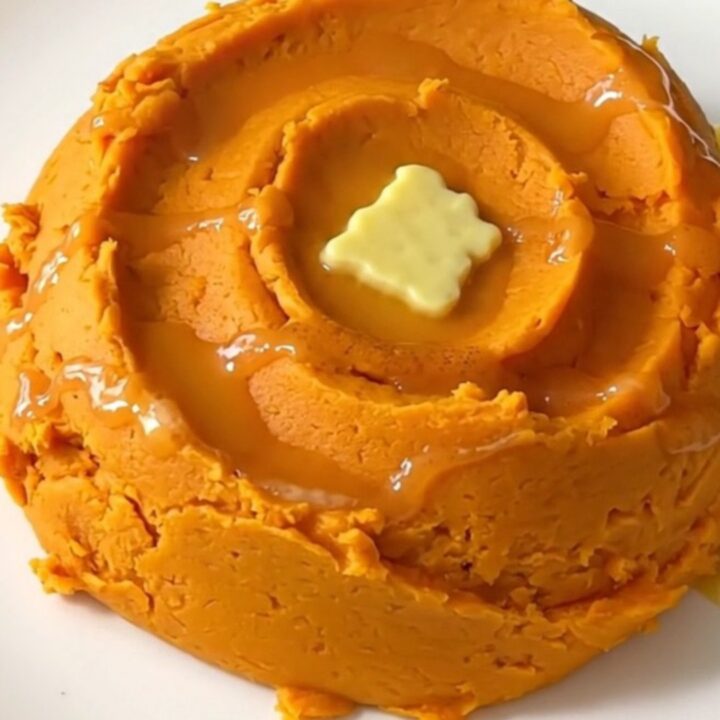 A mound of creamy, vibrant orange mashed sweet potatoes with cinnamon swirls in a ceramic bowl.