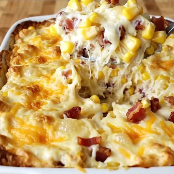A top-down view of a rectangular baking dish filled with corn, cream cheese cubes, and bacon before baking.