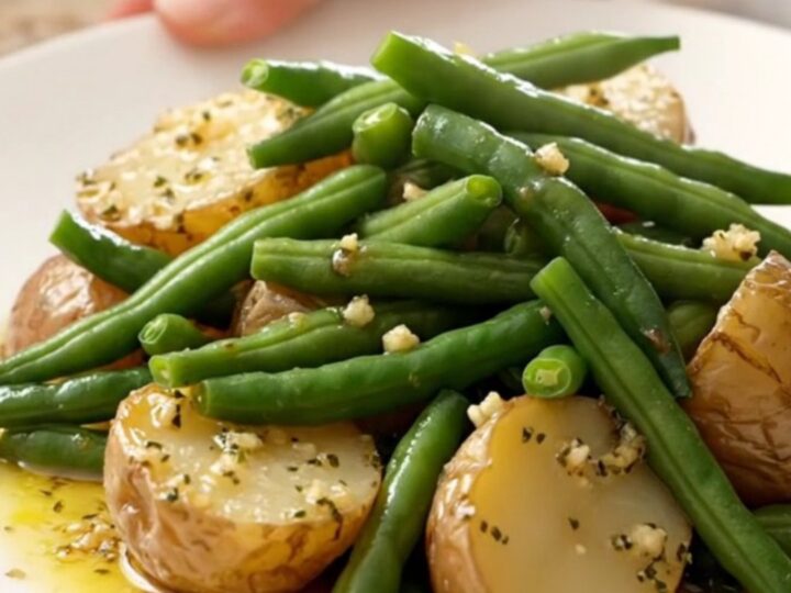 A close-up view of tender green beans and halved baby red potatoes in a garlic butter sauce inside a slow cooker.