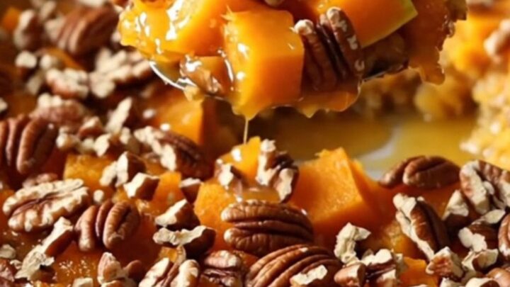 A ceramic baking dish filled with golden-brown roasted butternut squash cubes glazed in maple butter and topped with toasted