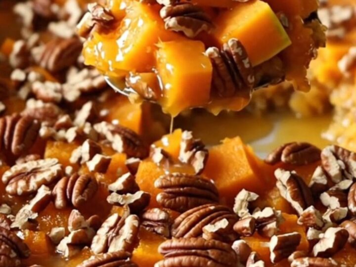 A ceramic baking dish filled with golden-brown roasted butternut squash cubes glazed in maple butter and topped with toasted
