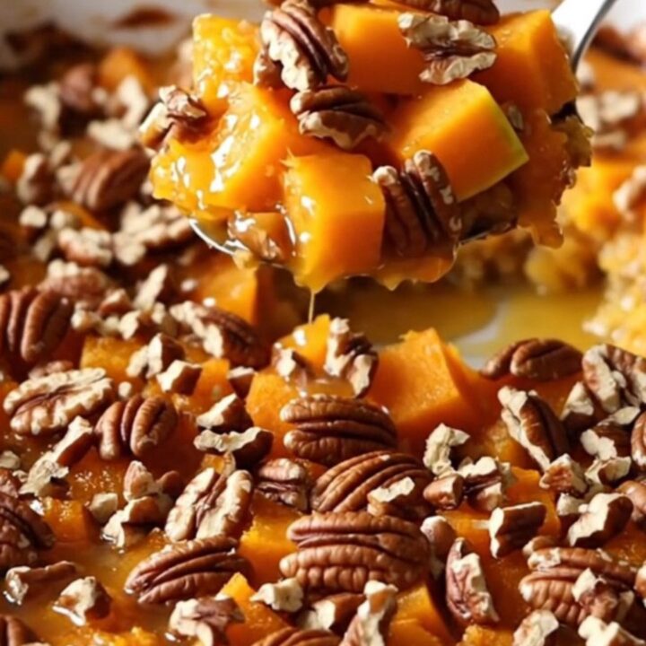A ceramic baking dish filled with golden-brown roasted butternut squash cubes glazed in maple butter and topped with toasted