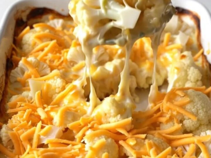 A golden, bubbling cheesy cauliflower gratin in a white rectangular ceramic dish on a white speckled surface.