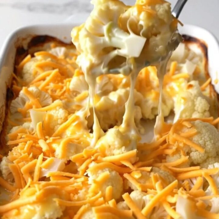 A golden, bubbling cheesy cauliflower gratin in a white rectangular ceramic dish on a white speckled surface.