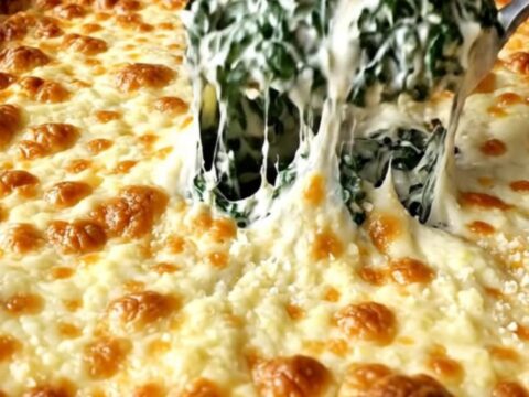 A top-down view of a creamy spinach bake in a rectangular ceramic dish, topped with bubbling golden mozzarella.