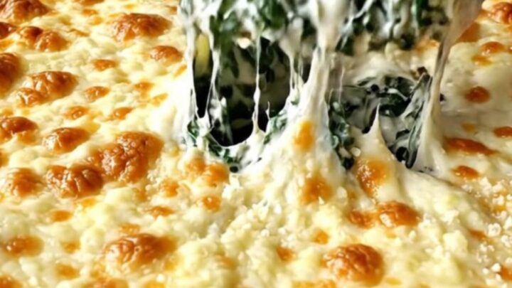 A top-down view of a creamy spinach bake in a rectangular ceramic dish, topped with bubbling golden mozzarella.