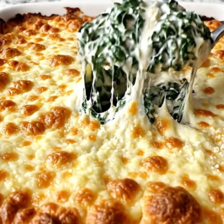 A top-down view of a creamy spinach bake in a rectangular ceramic dish, topped with bubbling golden mozzarella.