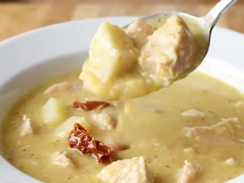 A shallow white bowl filled with creamy chicken and potato soup, garnished with herbs.