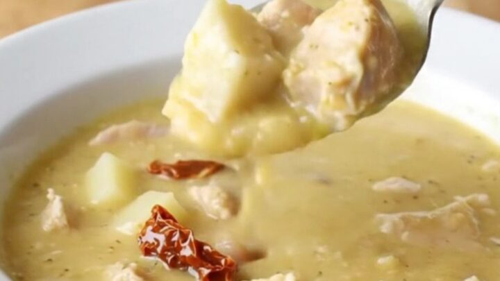 A shallow white bowl filled with creamy chicken and potato soup, garnished with herbs.