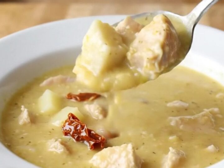 A shallow white bowl filled with creamy chicken and potato soup, garnished with herbs.
