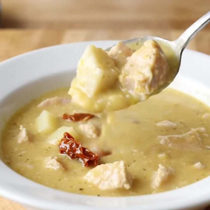 A shallow white bowl filled with creamy chicken and potato soup, garnished with herbs.