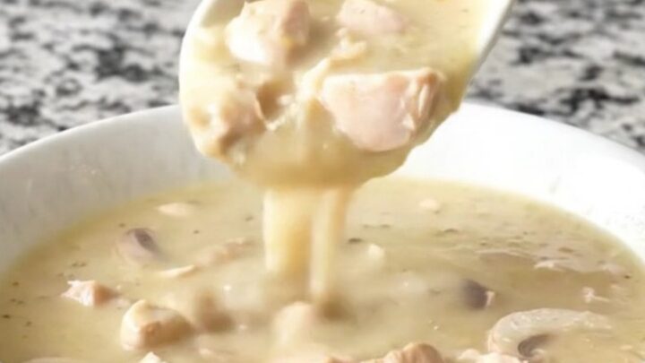 A close-up of a creamy chicken and mushroom soup in a white bowl with steam rising.