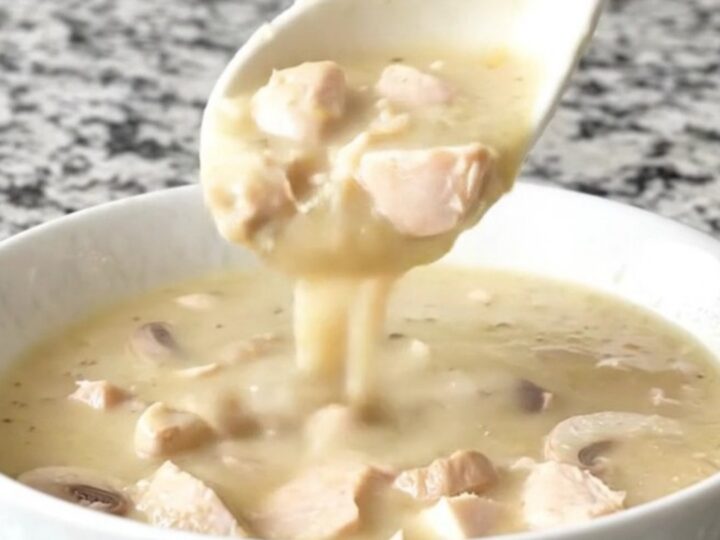 A close-up of a creamy chicken and mushroom soup in a white bowl with steam rising.