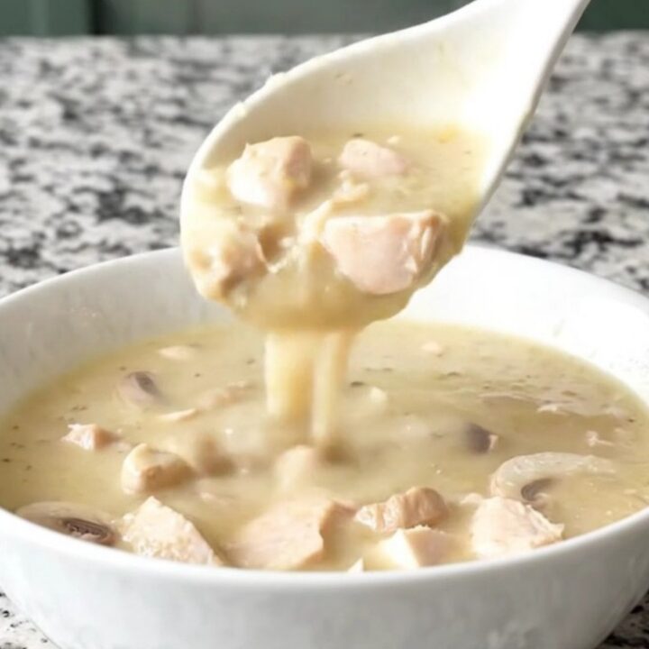 A close-up of a creamy chicken and mushroom soup in a white bowl with steam rising.